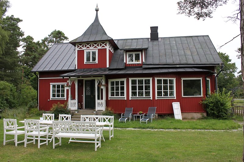 En unik rödvit trästuga med ett svart plåttak.