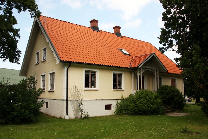 Ett ljusgult hus med röda fönster och ett rött tegeltak.