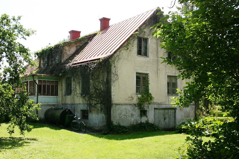 Ett bevuxet hus med röda fönster och ett rött plåttak.