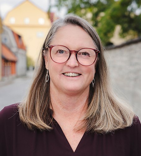 En kvinna med glasögon står framför en tegelvägg.