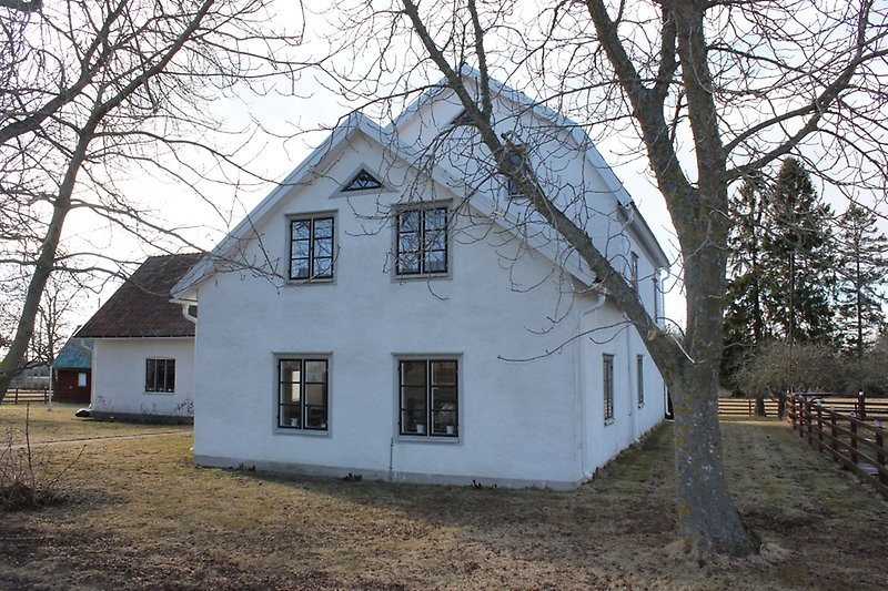 Ett vitt tvåvåningshus med svarta fönster och ett sadeltak.