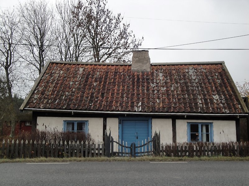 Ett litet hus som ligger längs vägen har ett rött tegeltak, blåa fönster och blå ytterdörr.