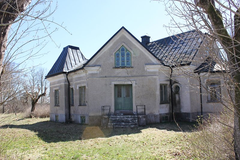 Ett vackert hus med ljusa väggar, ett svart tak, gröna fönster och grön ytterdörr.