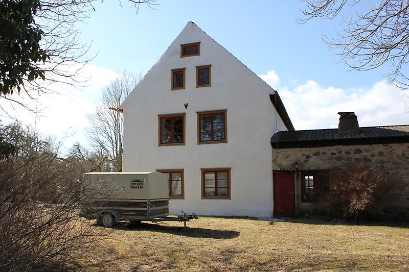 Ett vitt tvåvånings hus med röda fönster och ett svart plåttak.