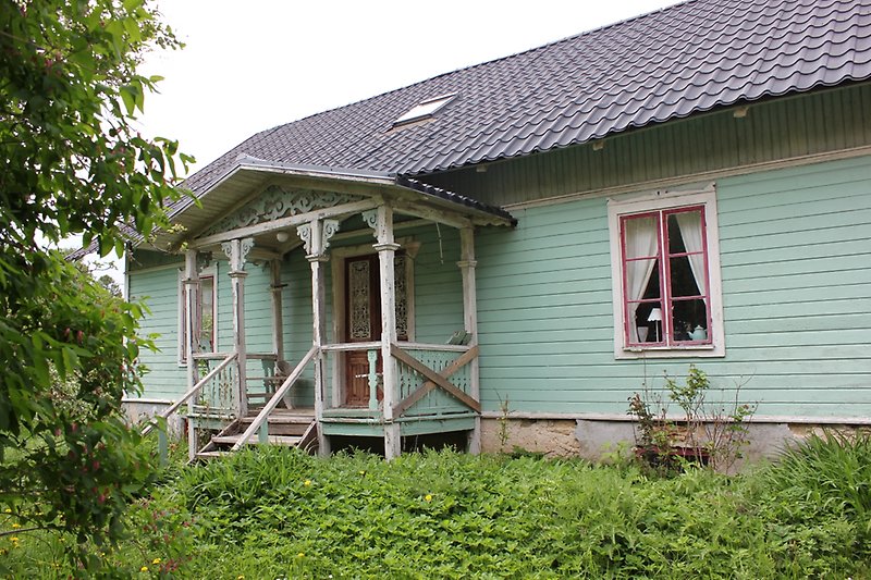 Ett grönt trähus med en brun ytterdörr, röda fönster och ett svart tak.