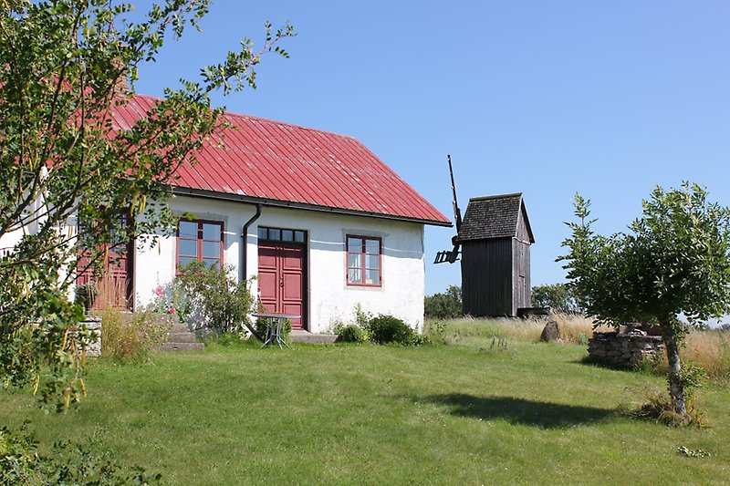 Ett vitt hus med rött tak, röda dörrar och fönster, längre bort syns det även en kvarn.