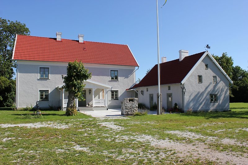 Två gråa hus med gröna fönster och klarblå himmel.
