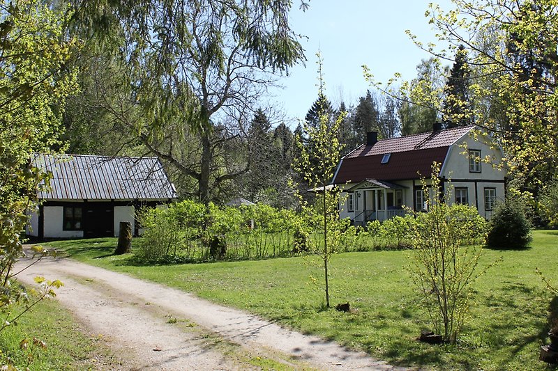 Tvåvånings hus med vita fönster, ett rött tak med två skorstenar, på gården finns det även ett gårdshus.