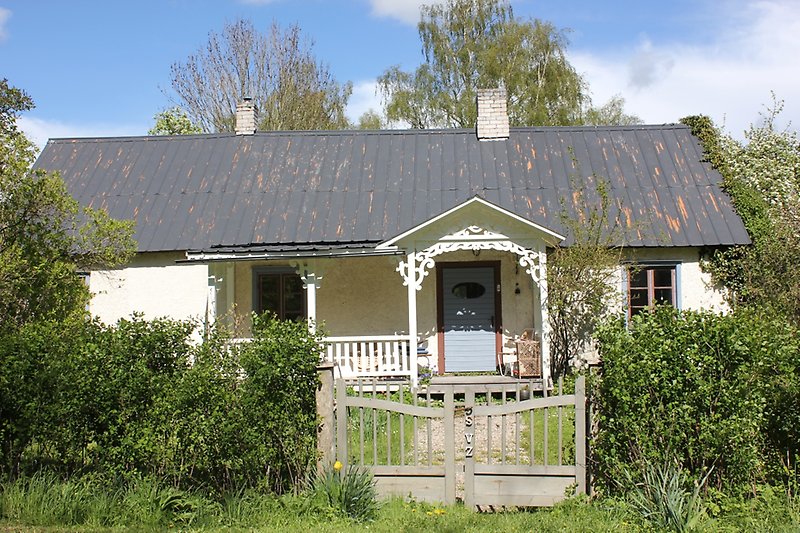 Ett vitt hus med bruna fönster, ett svart plåttak och en blå ytterdörr.