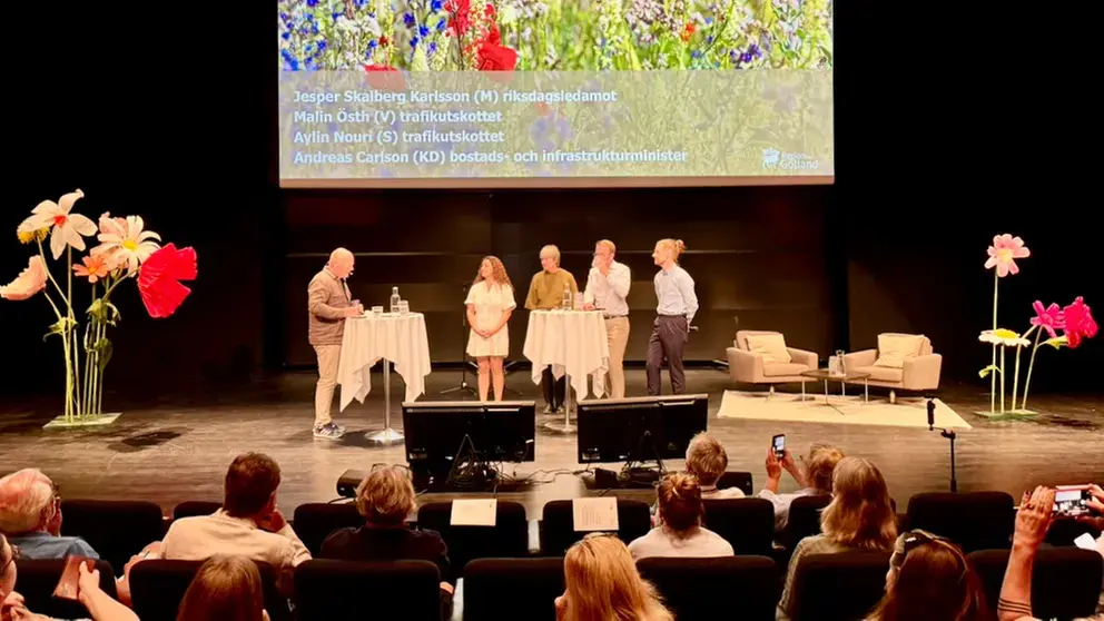 Personer på en scen med svart bakgrund och publik i förgrunden