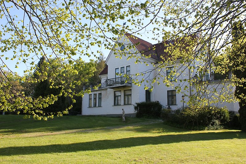 En vit villa av två våningar med gröna fönster och ett rött tak.
