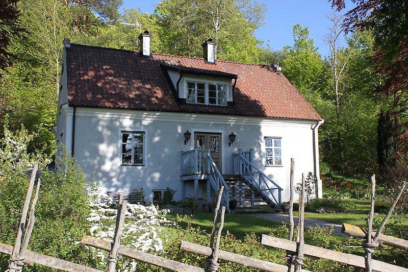 Envånings hus med vita väggar, ljusblåa fönster, ett rött tak och två skorstenar.
