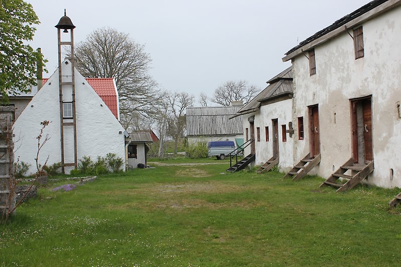 På höger sidan finns det en vit byggnad med trädörrar och röda fönster, på vänster sida finns det en vit byggnad med en ringklocka.