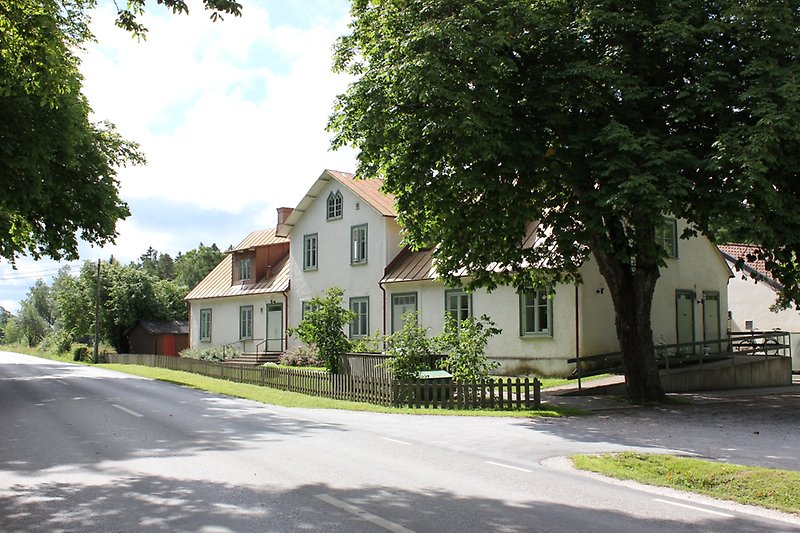 Ett stort vitt hus med olivgröna fönster och ett rött plåttak.