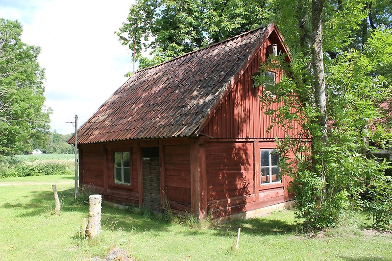 En röd trästuga med vita fönster och ett rött tegeltak.
