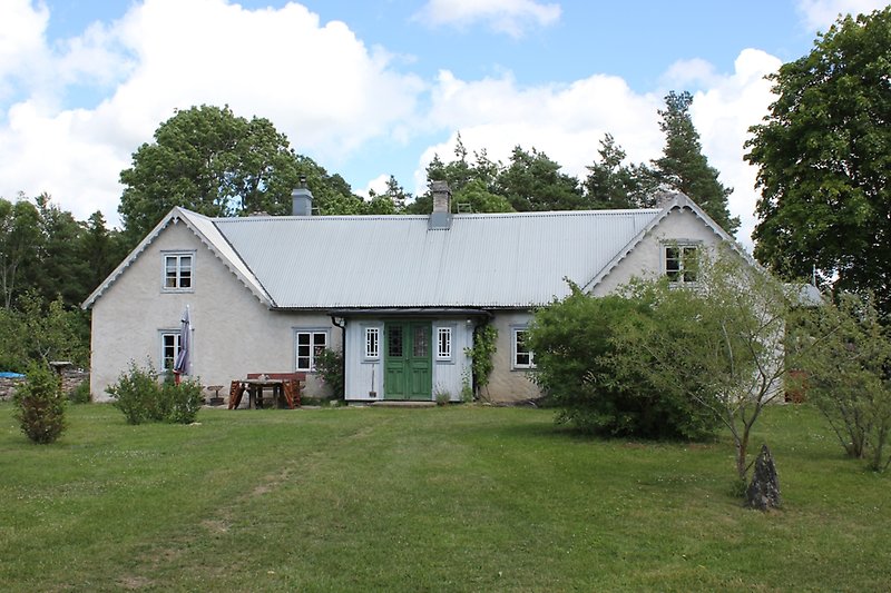 Ett vitt hus med en grön ytterdörr, vita fönster och ett grått plåttak med flera skorstenar.