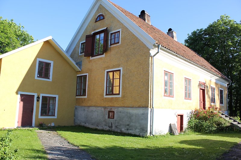 Ett gult hus med röda fönster, röda dörrar och ett rött tegeltak med två skorstenar.