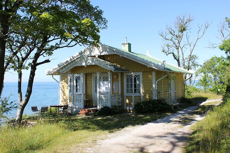 En gul stuga med vita fönster, en vit ytterdörr, ett grönt tak och en vacker utsikt över havet.