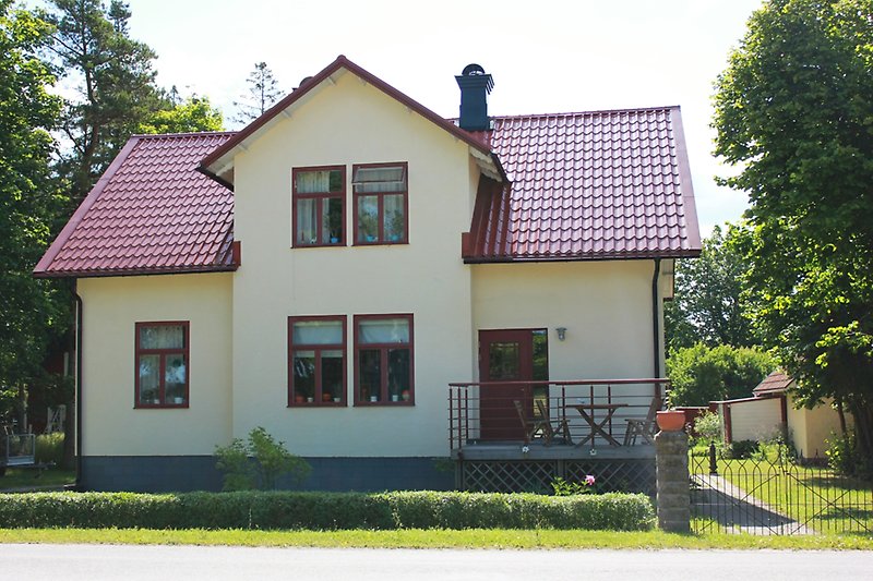 Ett vitt hus med röda fönster, en röd ytterdörr och ett rött tak.