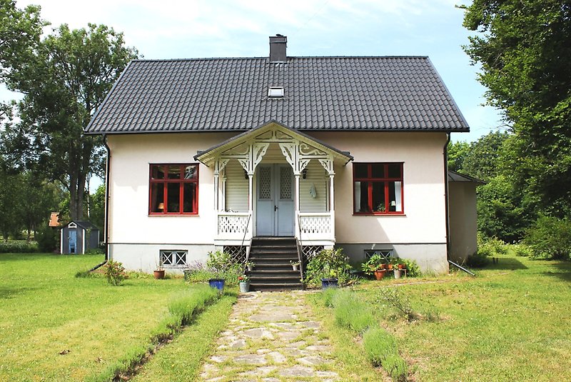 Ett vitt hus med en blå ytterdörr, röda fönster och ett svart tak.