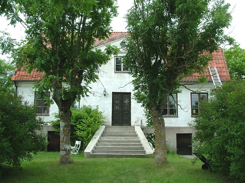 Ett vitt hus med en svart ytterdörr, svarta fönster och ett rött tegeltak.