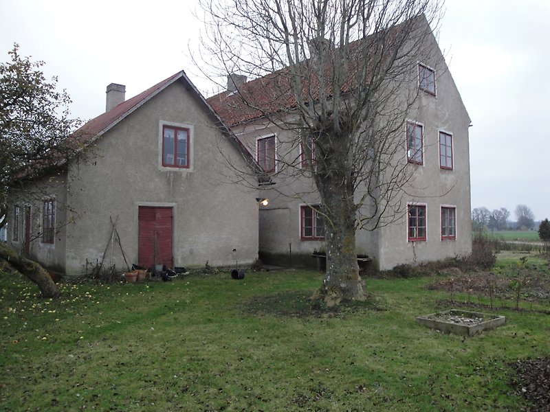 Två gråa hus med rödbruna tegeltak, röda dörrar och fönster.