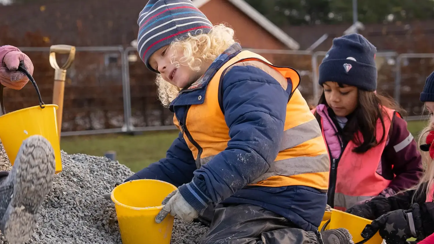 Barn med hink och reflexväst som leker i grushög