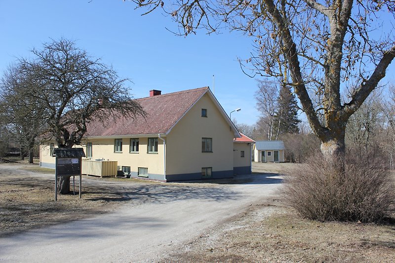 Ett gult envåningshus med gröna fönster och ett rött tak.