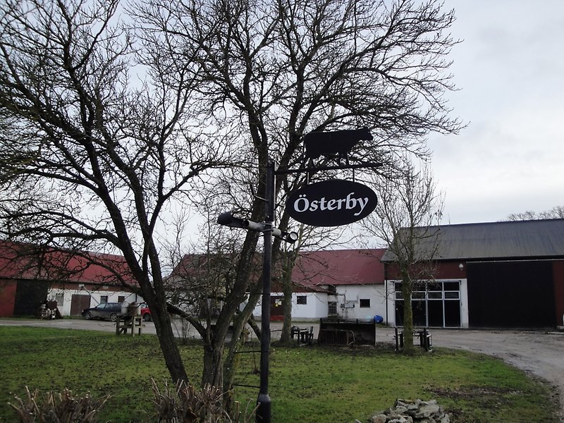 Flera byggnader med röda plåttak längre bak och på mitten av innegård syns en upphängd skylt med Österby på