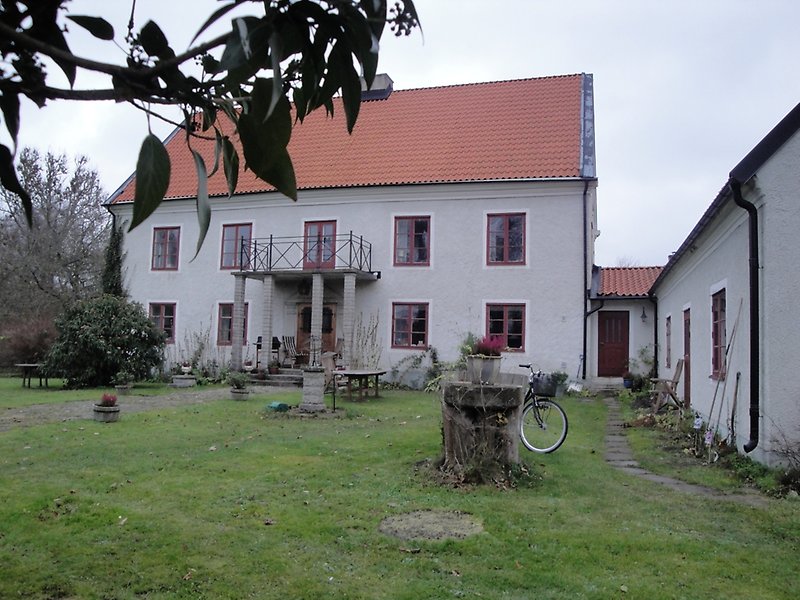 Ett vitt hus med röda fönster, brun ytterdörr och ett rött tegeltak med en skorsten.