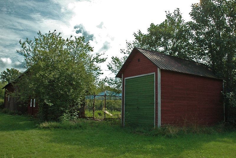 En röd liten träbod med en grön ytterdörr och ett svart sadeltak.