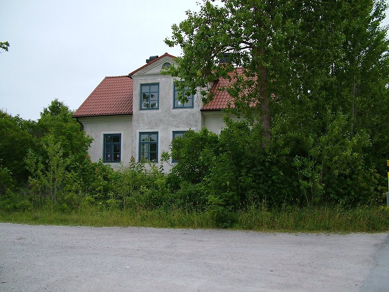 Ett vitt tvåvåningshus med blåa fönster och ett rött tak.