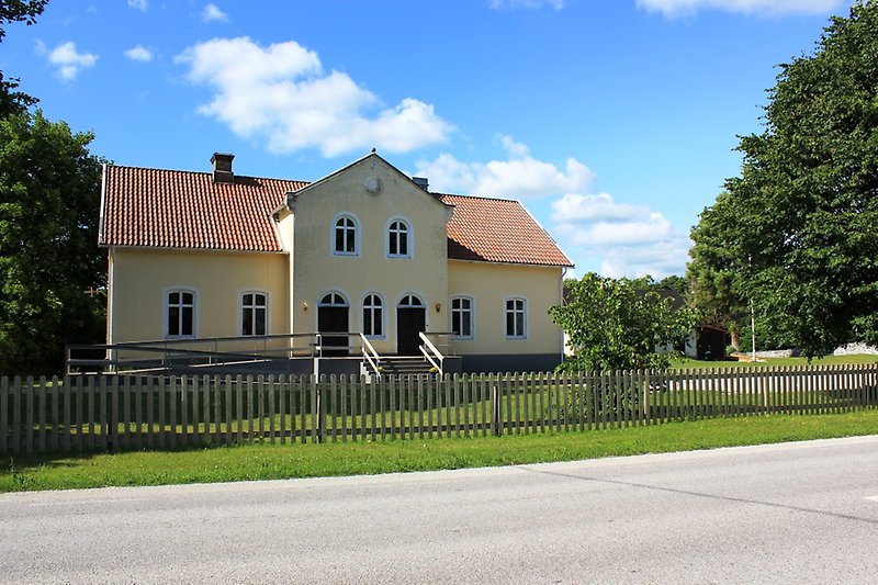 En gul byggnad med vita fönster, svarta dörrar och ett rött tegeltak.